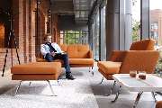 Büro-Creativ GmbH - Büro- & Objekteinrichtung - Ein stilvoll eingerichteter Loungebereich mit modernen Sitzmöbeln in warmen Farbtönen. Die harmonische Kombination aus industriellen Elementen, großzügigen Glasflächen und gemütlichen Polstermöbeln schafft e