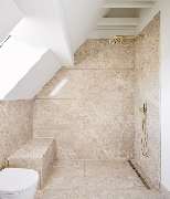Carolin Dißmann Architektur GmbH | Architektin München - Hochwertig ausgestattetes Duschbad unter der Dachschräge mit Natursteinverkleidung, goldenen Armaturen und integrierter Sitzbank. Eine Kombination aus Funktionalität und eleganter Zurückhaltung.