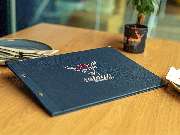 Das Blümchen | Restaurant Friedrichshafen - Speisekarte mit Logo des Restaurants Das Blümchen Friedrichshafen auf Holztisch – elegantes Design im Stil moderner Schwarzwald-Tapas.