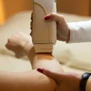 Derma First Cosmetics - Das Bild zeigt eine Kosmetikerin, die einen Epilierer verwendet, um feine Haare auf dem Unterarm einer Kundin zu entfernen. Der Arm liegt stabil, während das Gerät präzise über die Haut geführt wird. Die Szene wirkt professionell, 