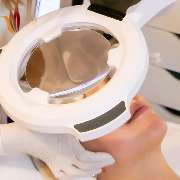 Derma First Cosmetics - Kundin in einem Kosmetikstudio liegt entspannt auf einer Behandlungsliege, während eine professionelle Kosmetikerin eine Hautpflegebehandlung durchführt. Über der Kundin befindet sich ein Vergrößerungsglas, das präzises Arbeiten an