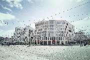 Dermatologikum Bremen - Moderne Außenansicht eines mehrstöckigen Gebäudekomplexes mit Glasfassade und klarer Architektur im Zentrum einer Stadt. Zahlreiche Menschen bewegen sich vor dem Gebäude, das Geschäfte im Erdgeschoss und Praxisräume in den oberen E