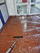 E&E Gebäudereinigung - E&E Gebäudereinigung Gründliche Bodenreinigung eines roten Fliesenbodens, bei der Schmutz und Reinigungsrückstände mit einem Absauggerät entfernt werden, um eine saubere und gepflegte Oberfläche zu erzielen.