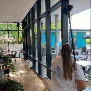 Fein Gebäude-Service - Eine Mitarbeiterin reinigt mit einem Teleskopstab große Glasfenster eines stilvoll eingerichteten Gastraums mit Ausblick auf den Außenbereich.