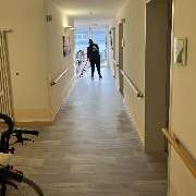 Fein Gebäude-Service - Eine Mitarbeiterin von Fein Gebäude-Service reinigt sorgfältig den Boden in einem hellen Flur mit Haltegriffen – eine Umgebung, die auf barrierefreie Pflegeeinrichtungen hinweist.