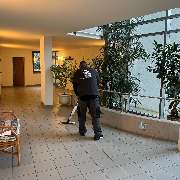 Fein Gebäude-Service - Eine Reinigungskraft bei der Arbeit in einem hellen, begrünten Flurbereich eines Gebäudes mit Sitzgelegenheiten.