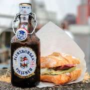 Bügelverschlusflasche mit Flensburger Pilsener neben einem Fischbrötchen am Flensburger Hafen.