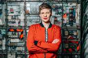 Julia Reisinger Fotografie - Julia Reisinger Fotografie Ein modernes Portrait einer Frau in auffälliger roter Jacke, aufgenommen vor einer urbanen, technischen Kulisse für einen markanten Look.
