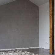 Ein fugenlos, gespachtelter Designboden, eine individuelle Wandfläche in moderner Betonoptik in Kombination mit wevet-weißen Wandflächen und geölten Holzbalken aus dem Altbestand, verleihen diesem neu ausgebauten Dachgeschoß ein anmutendes Loft-Ambiente.