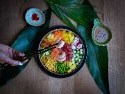 MAUI - Hawasian & Vietnamese Restaurant | München Ludwigpalais - Bunte Poké Bowl mit Garnelen, Mais, Edamame, Mango und Karotten – liebevoll serviert auf tropischen Blättern mit Dips und Stäbchen.