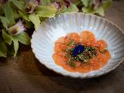 MAUI - Hawasian & Vietnamese Restaurant | München Ludwigpalais - Fein angerichtetes Lachstatar in Blütenform mit Kaviar und Blüte, serviert auf weißem Teller mit dekorativen Orchideen im Hintergrund.