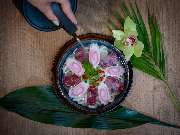MAUI - Hawasian & Vietnamese Restaurant | München Ludwigpalais - Kunstvoll angerichtetes Dessert mit rosa Blüten-Optik, serviert in einer schwarzen Schale auf tropischem Blatt – stilvoll ergänzt durch eine Orchidee und Hand mit Löffel.