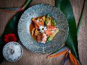 MAUI - Hawasian & Vietnamese Restaurant | München Ludwigpalais - Stilvoll angerichtetes Asia-Gericht mit Lachsfilet, Gemüse, Reis und essbaren Blüten – exotisch präsentiert auf grün-blauem Teller und tropischem Untergrund.