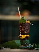 MAUI - Hawasian & Vietnamese Restaurant | München Nymphenburg - Exotischer Tiki-Cocktail im verzierten Becher mit Limette, Minze und Trinkhalm – stimmungsvoll angerichtet auf tropischem Blatt.
