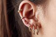 OMEN Tattoo & Piercing - Berlin Mitte - Detailaufnahme eines Ohrs mit mehreren goldenen Piercings in unterschiedlichen Formen und Positionen.