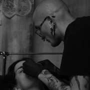 OMEN Tattoo & Piercing - Berlin Mitte - Piercer mit Brille und Tattoos arbeitet konzentriert an einem Gesichtspiercing einer Person im Studio.