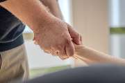 Physiotherapie Human-Health-Concepts - by Andreas Koch - Das Bild zeigt eine krankengymnastische Behandlung, bei der der Therapeut das Handgelenk des Patienten mit beiden Händen stabilisiert und bewegt.