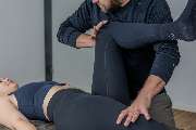 Physiotherapie Human-Health-Concepts - by Andreas Koch - Das Bild zeigt eine physiotherapeutische Anwendung mit kinesiologischen Elementen, bei der der Therapeut gezielt mit den Beinen des Patienten arbeitet.