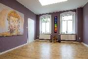 Physiotherapie Praxis Stefan Arnhold - Ein geräumiger und ruhiger Meditations- und Entspannungsraum mit violetten Wänden und hellem Holzboden. Links an der Wand hängt ein großformatiges Gemälde eines Buddha-Kopfes in warmen Gold- und Beigetönen mit einem 