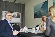 proJob Personal- und Unternehmensberatung GmbH - Das Bild zeigt eine Recruiting-Situation in einem modernen Büro in Köln. Drei Personen sitzen an einem Besprechungstisch, umgeben von Unterlagen, Getränken und einem großen Bildschirm im Hintergrund.