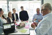 proJob Personal- und Unternehmensberatung GmbH - Das Bild zeigt eine typische Szene aus einem Teambuilding-Workshop bei proJob in Köln. Sechs Personen stehen um einen Tisch in einem modernen Büro und arbeiten gemeinsam mit farbigen Haftnotizen, Stiften un