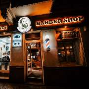 The Barber Yard Barber Shop in Berlin-Neukölln bei Nacht – stilvolle Fassade mit beleuchteter Beschilderung.