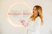 Westhafen Beauty - Westhafen Beauty Eine Expertin hält ein Behandlungsinstrument und steht vor einer dekorativen Wandbeleuchtung, bereit für die nächste Hautpflegebehandlung.